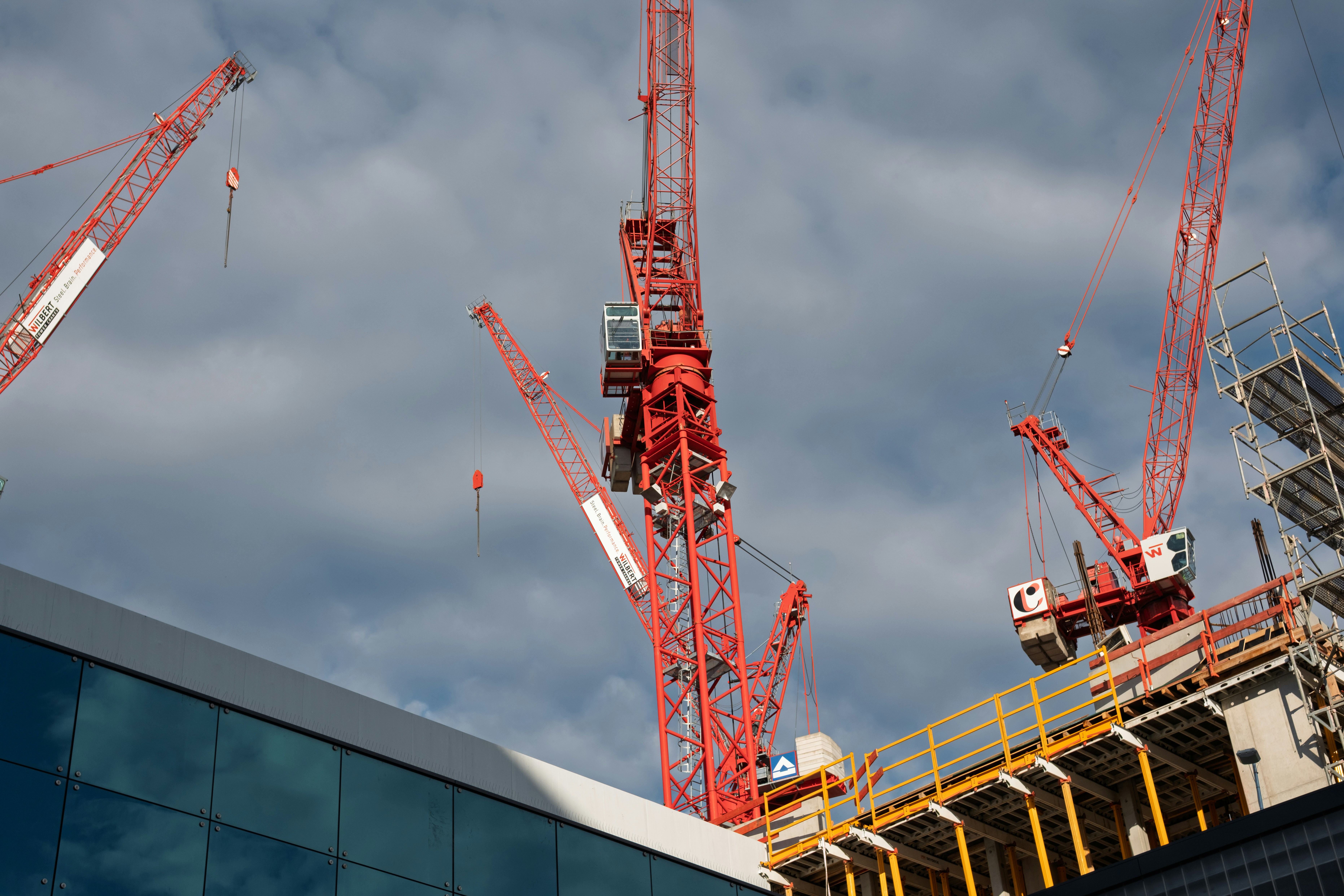 Rote Baukräne vor einem wolkenverhangenen Himmel.