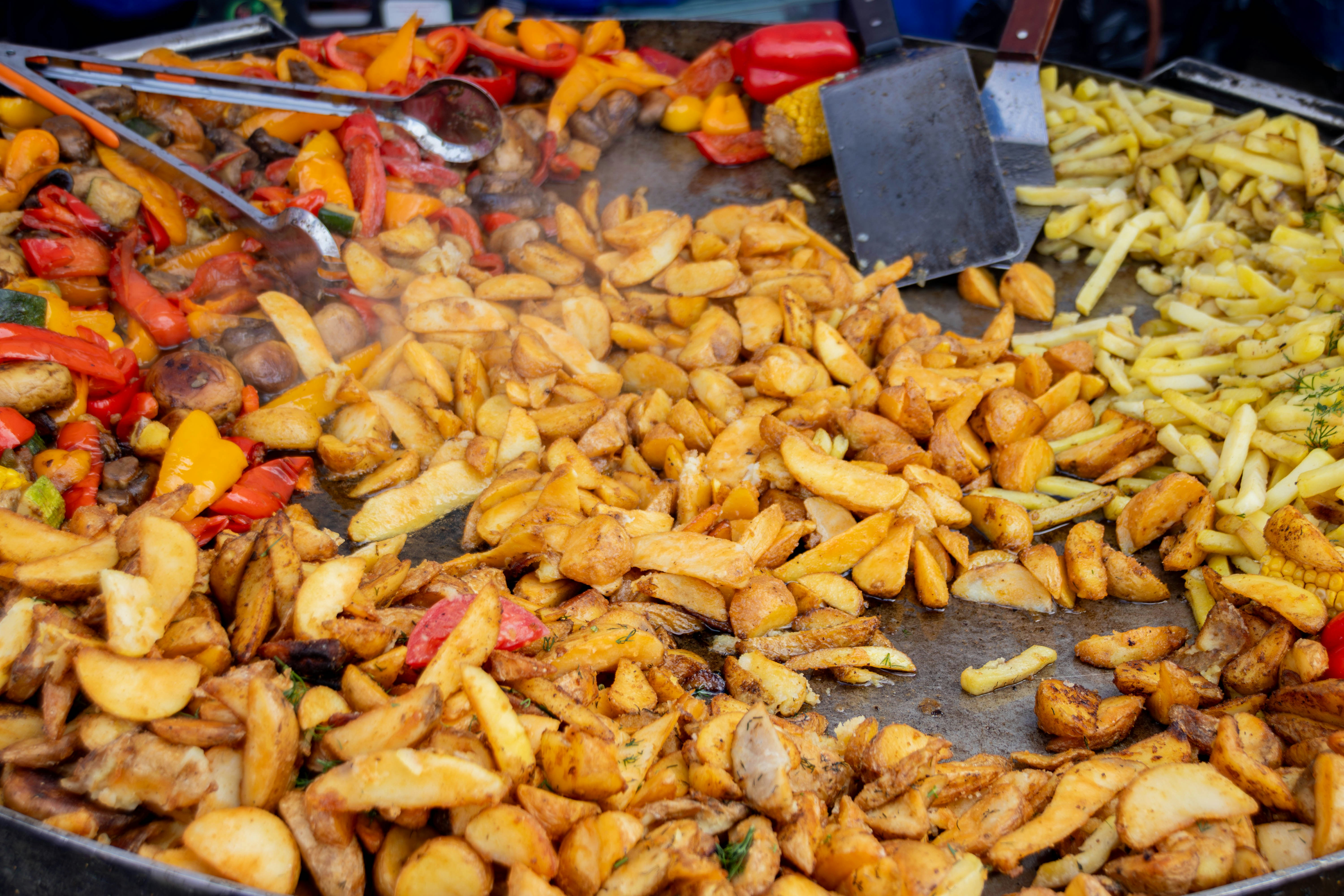 Fried potatoes and peppers cooking on a large griddle.