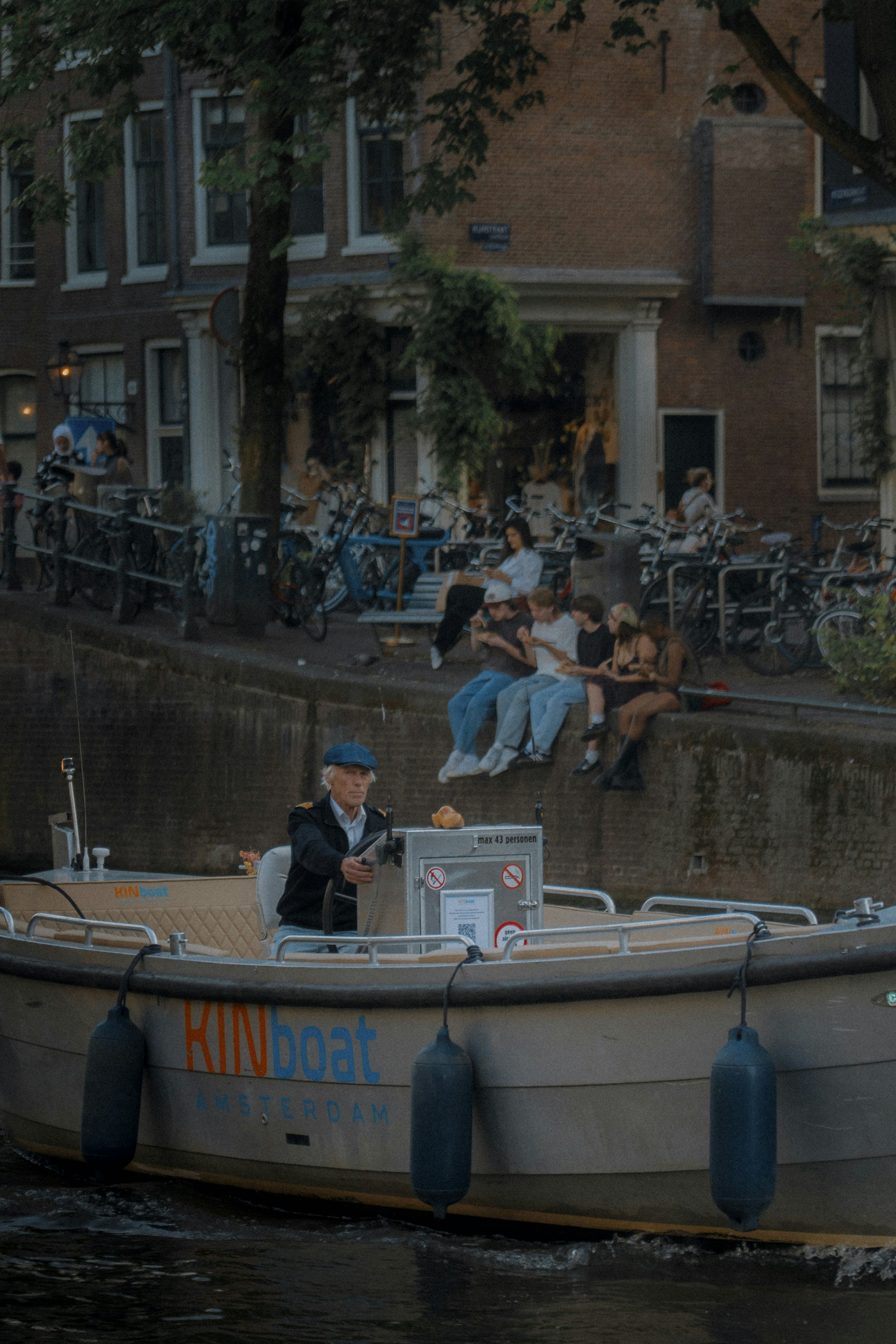 Man steers boat down amsterdam canal with people watching