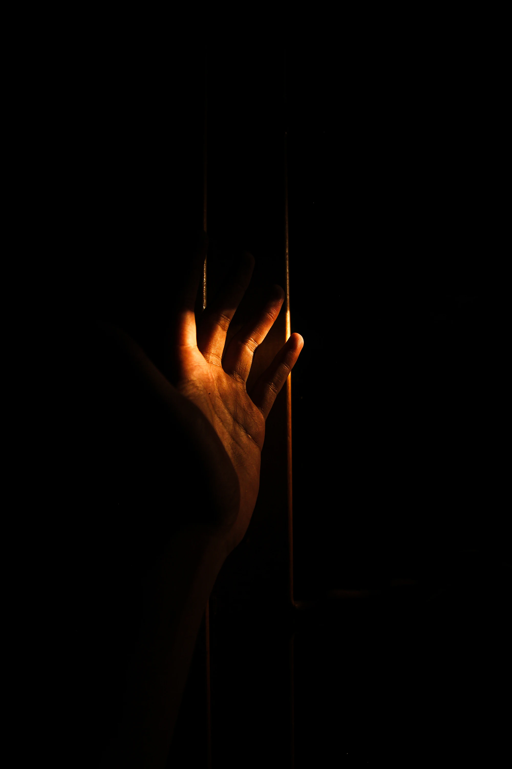 A hand emerging from darkness into a narrow shaft of warm light