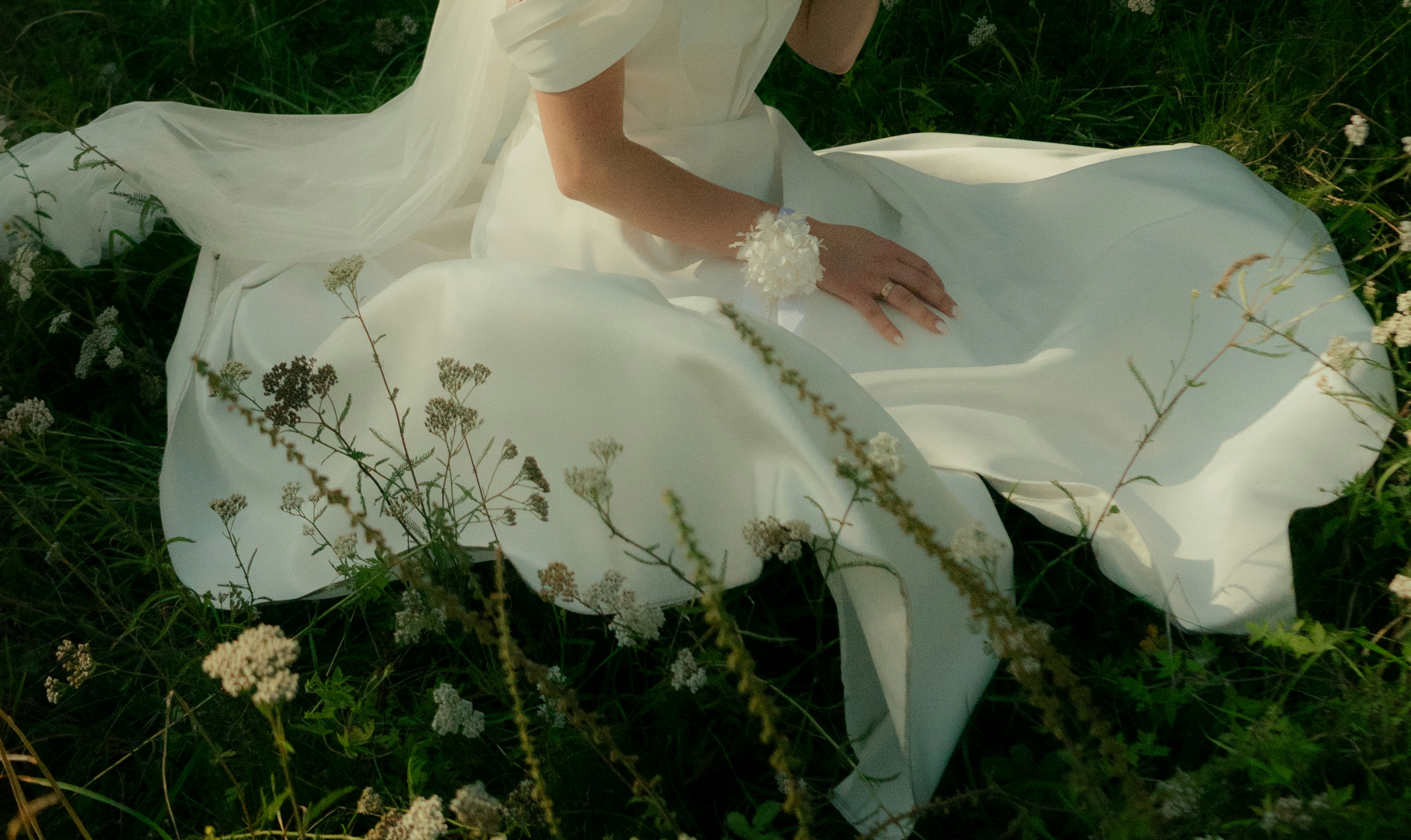 Elegant Bride in a Flowing White Gown Seated in a Serene Meadow