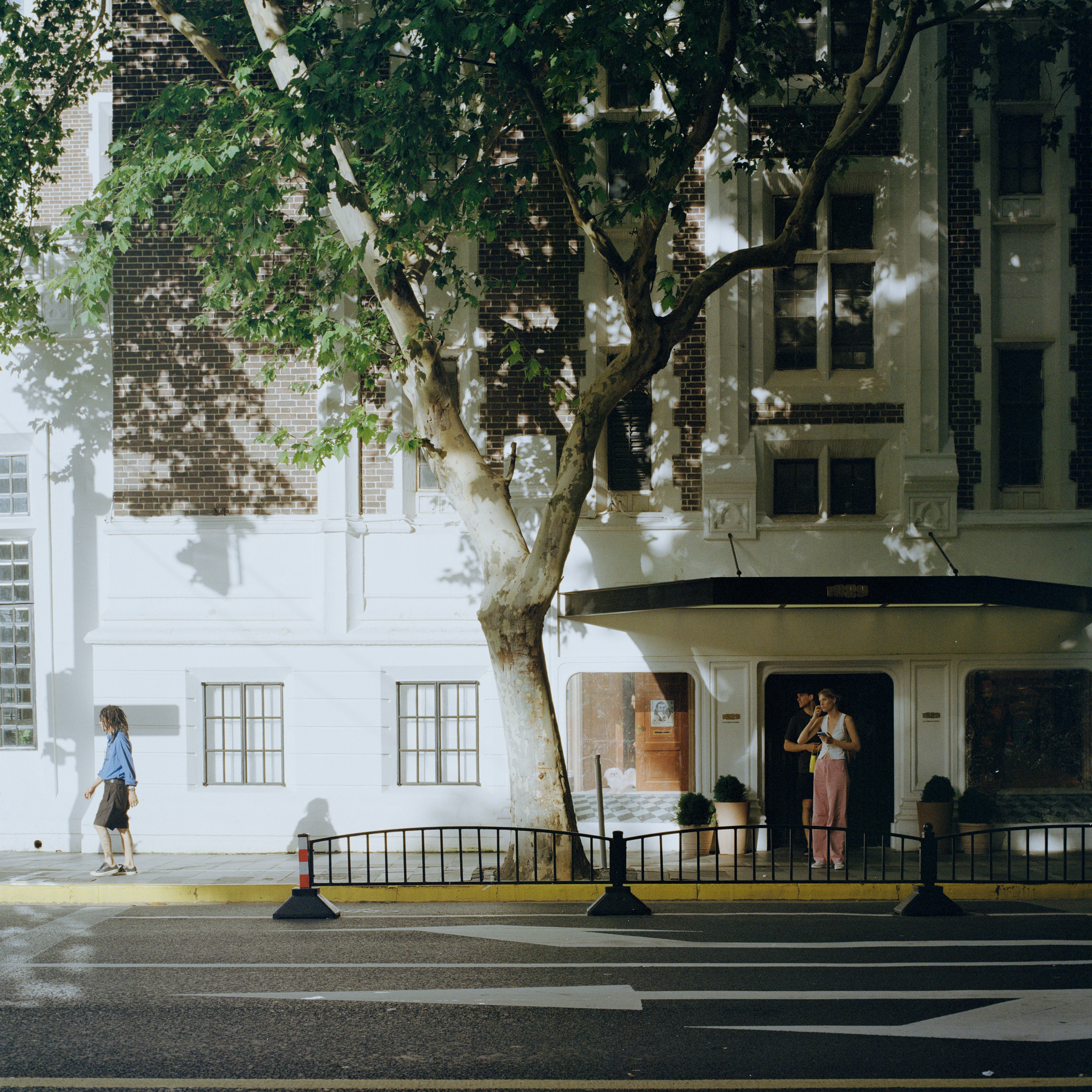 Woman walking past building with tree and entrance