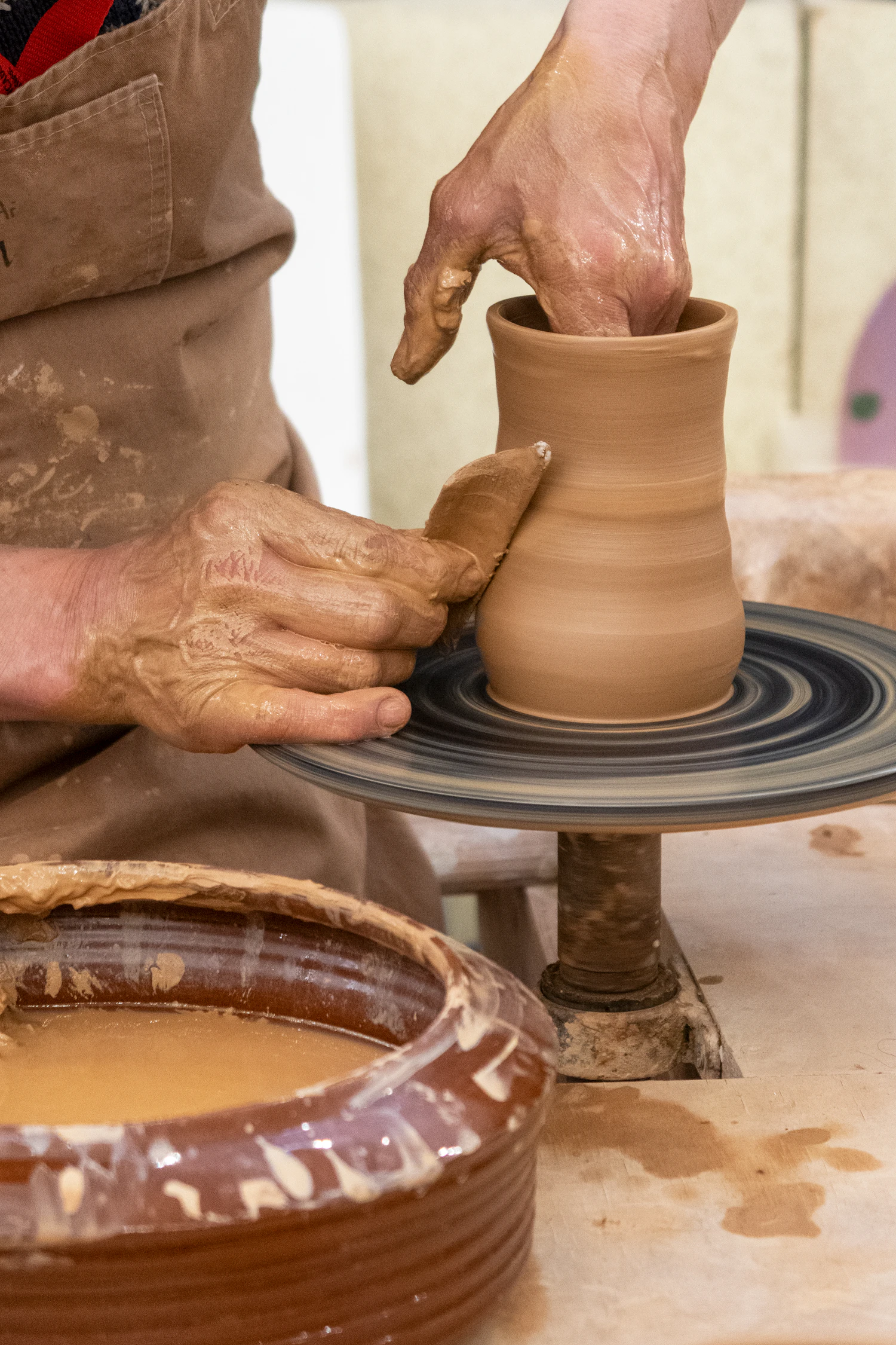A potter pulling the wall of a jug upward on a spinning wheel