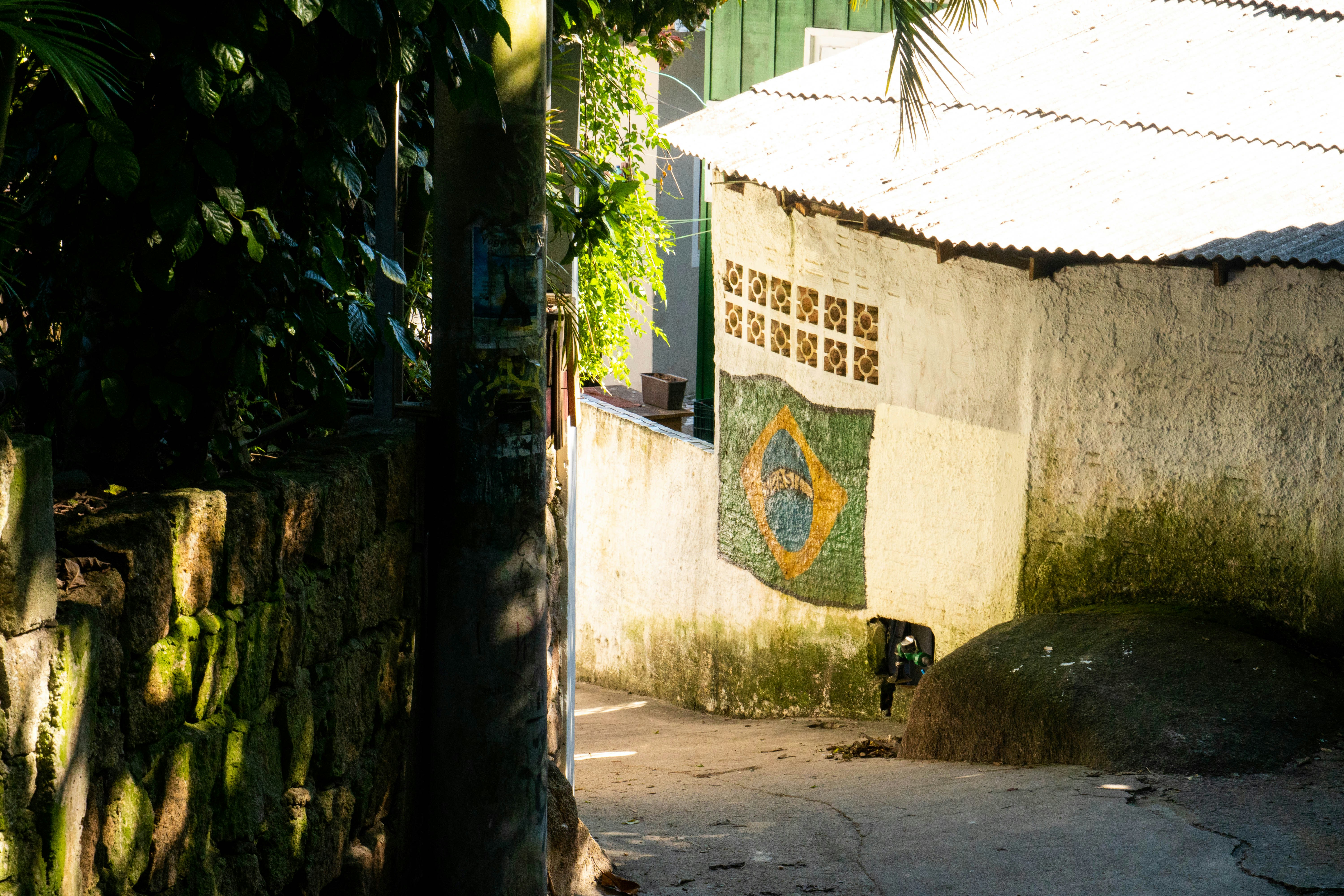 Brazilian flag hangs on a wall in a sunny alley.