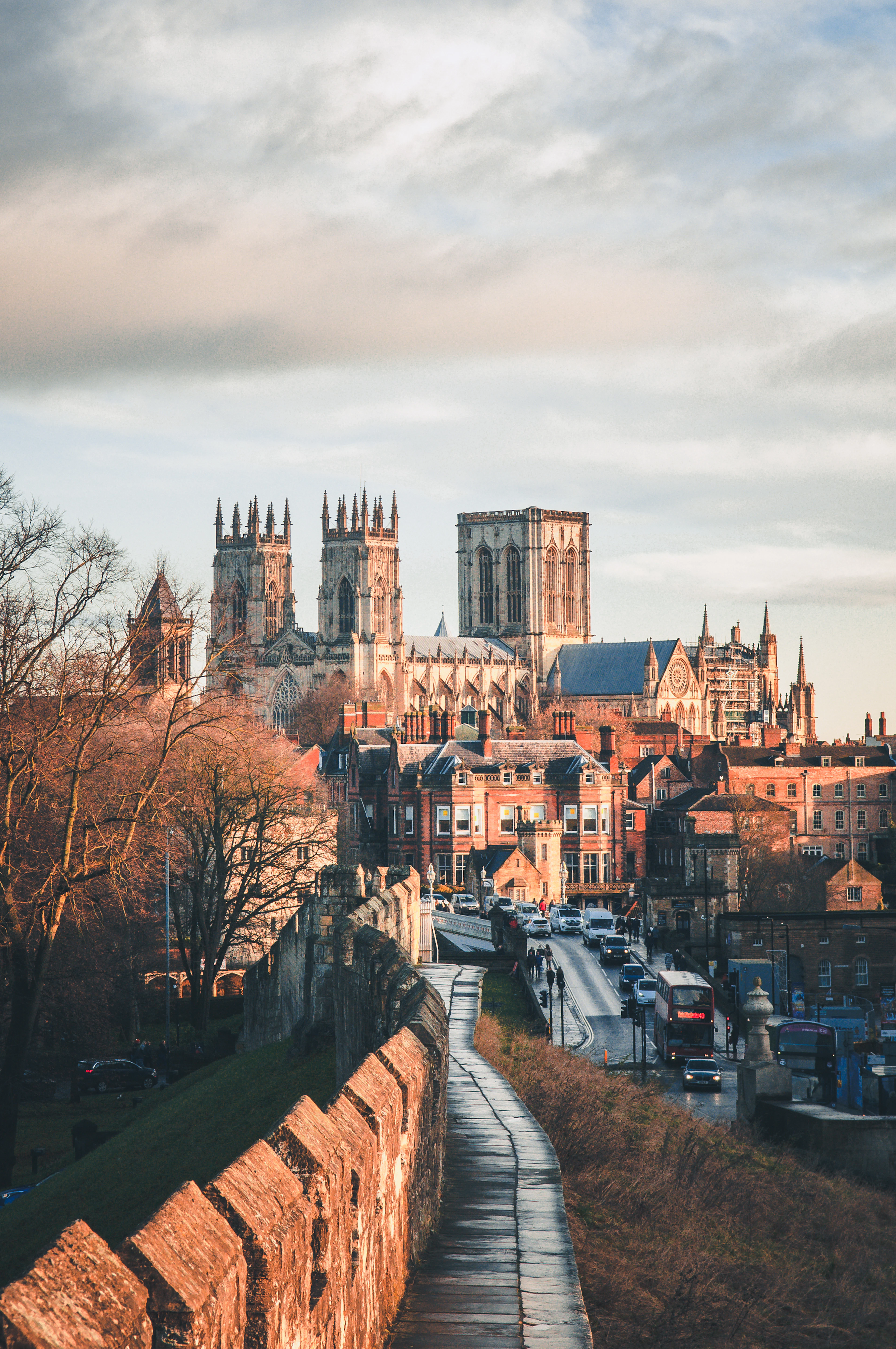 The stone walkway along York's medieval city walls curving away in low golden light, red-brick rooftops below and the towers of York Minster rising beyond.