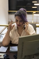 Woman with purple hair talking on phone at desk.