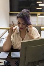 Woman with purple hair talking on phone at desk.
