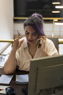 Woman with purple hair talking on phone at desk.