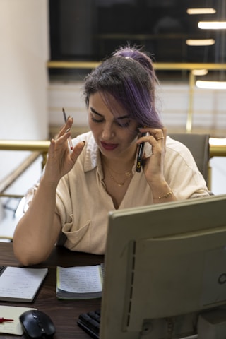 Woman with purple hair talking on phone at desk.