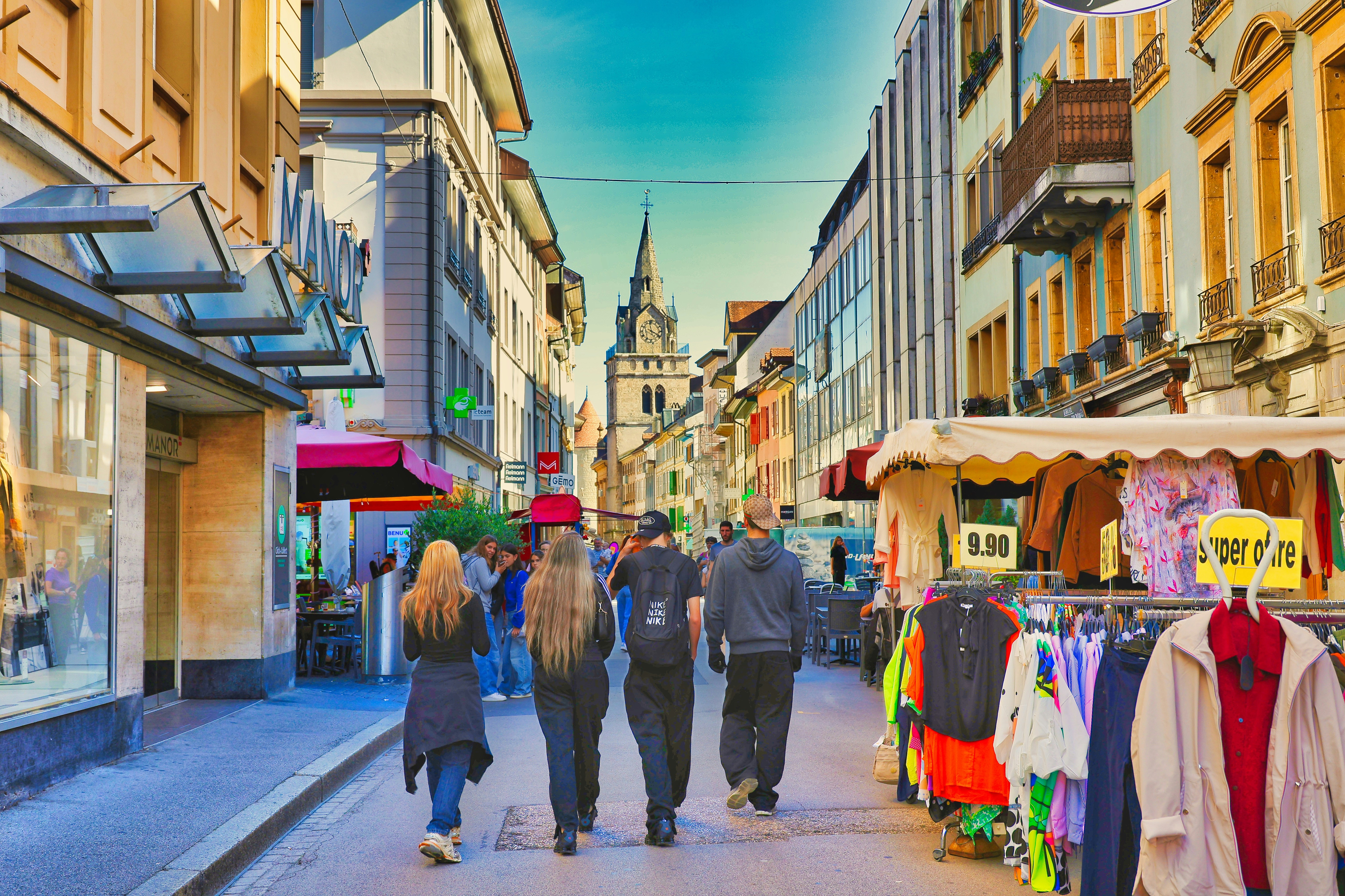 People walk down a sunny european street with shops.