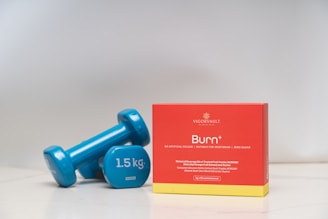 Two blue dumbbells and a box of burn supplement.