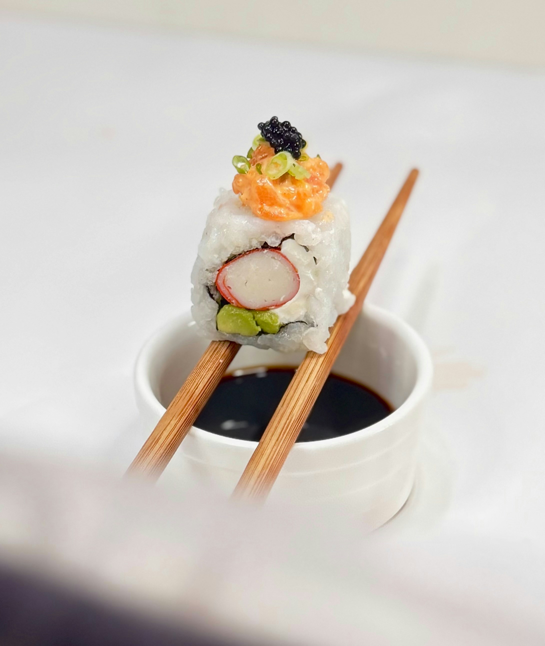 A single sushi roll held by chopsticks over soy sauce.
