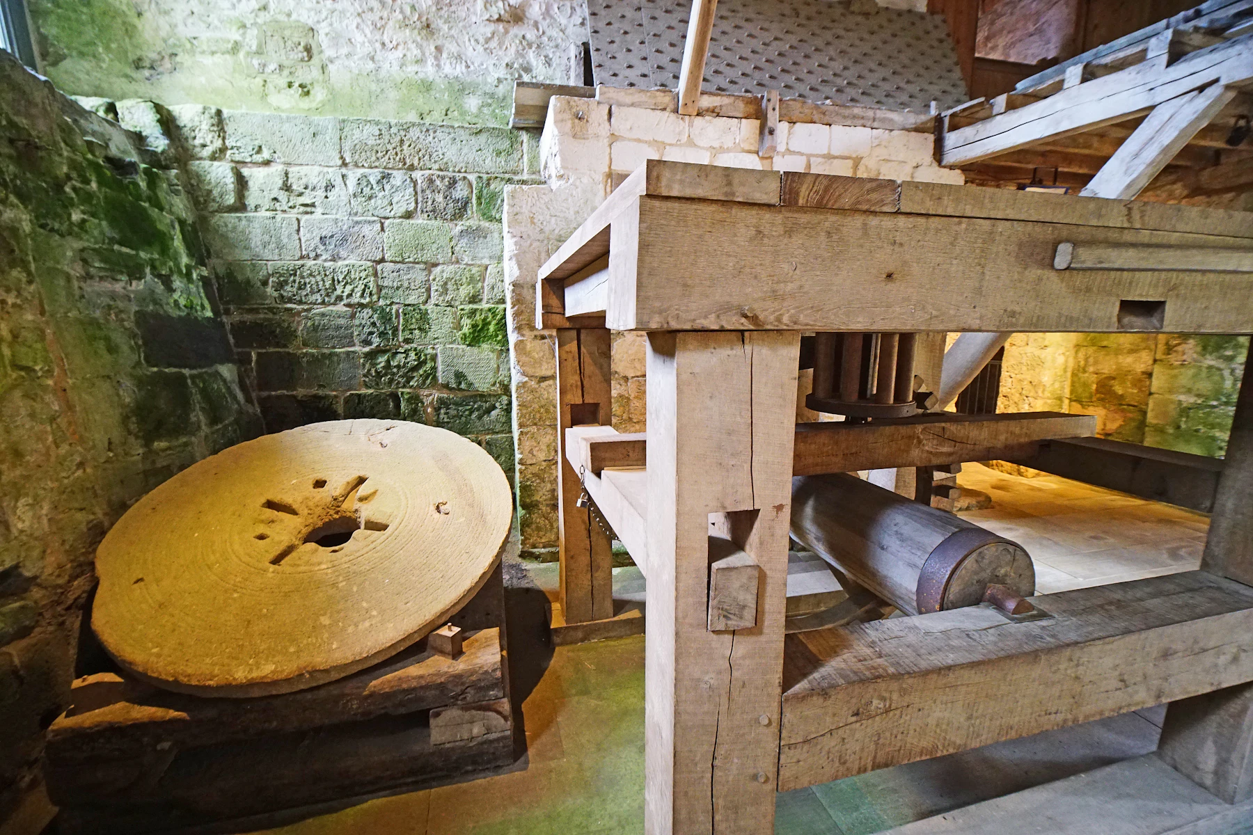 An old runner millstone beside a heavy wooden frame inside a stone mill house