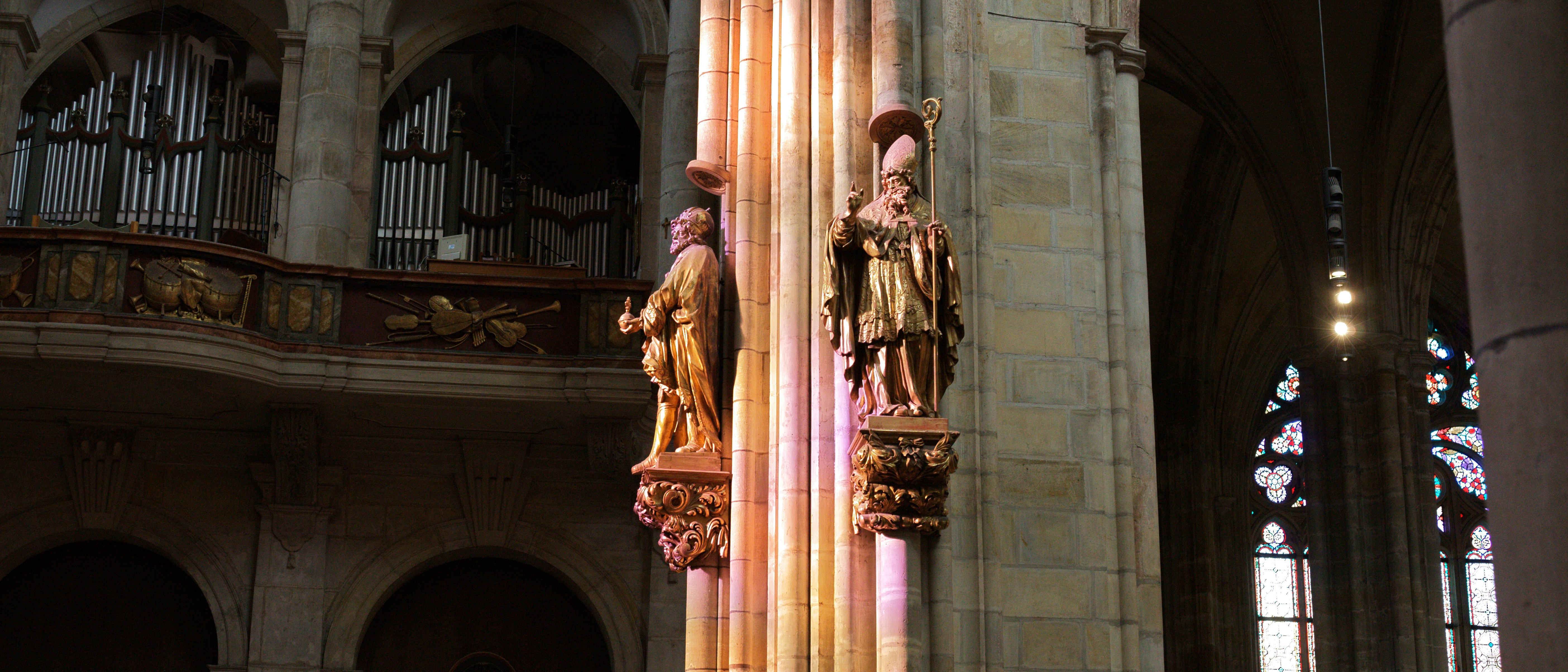 Two ornate statues adorn a cathedral pillar with stained glass.