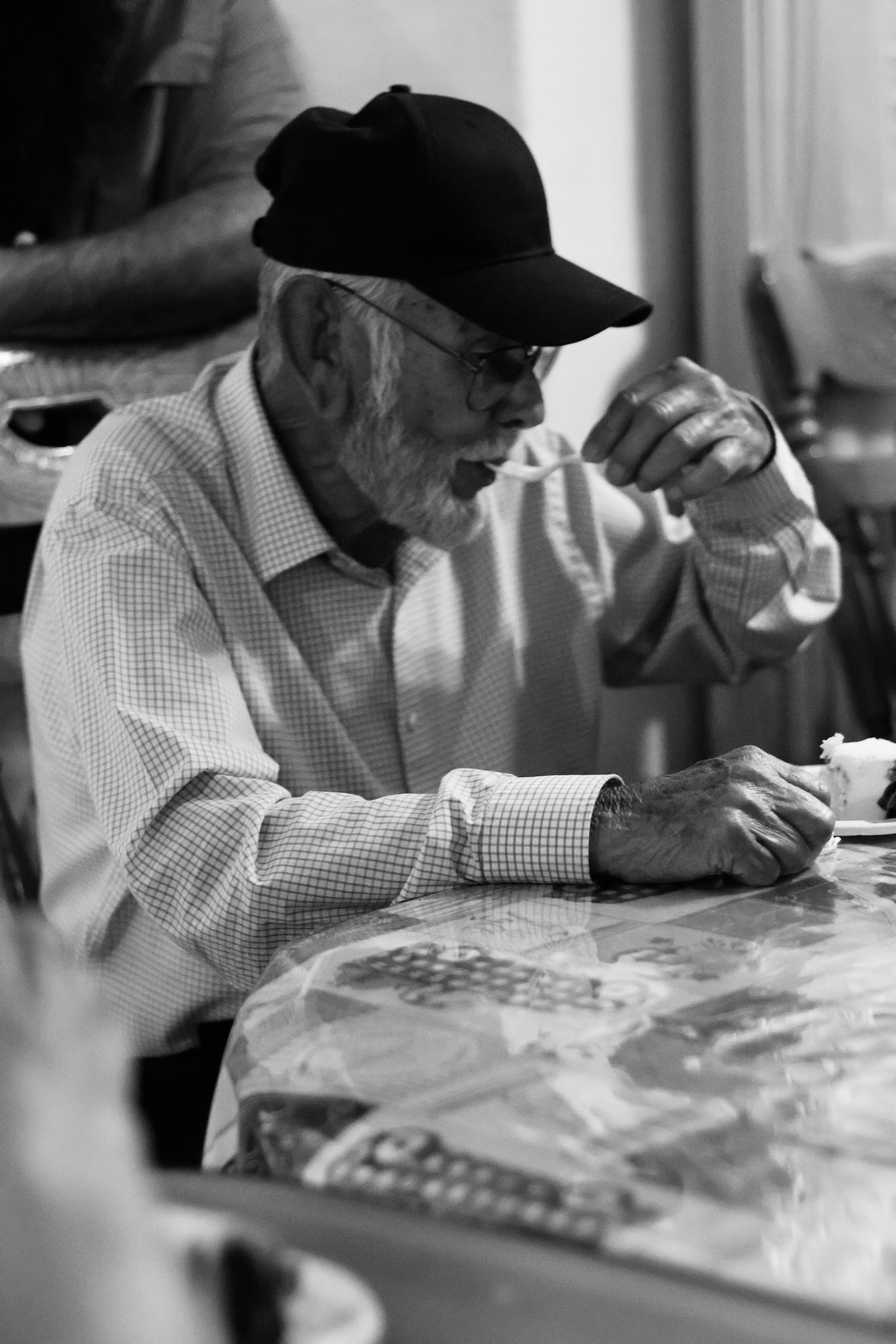 Elderly man in baseball cap eating at table
