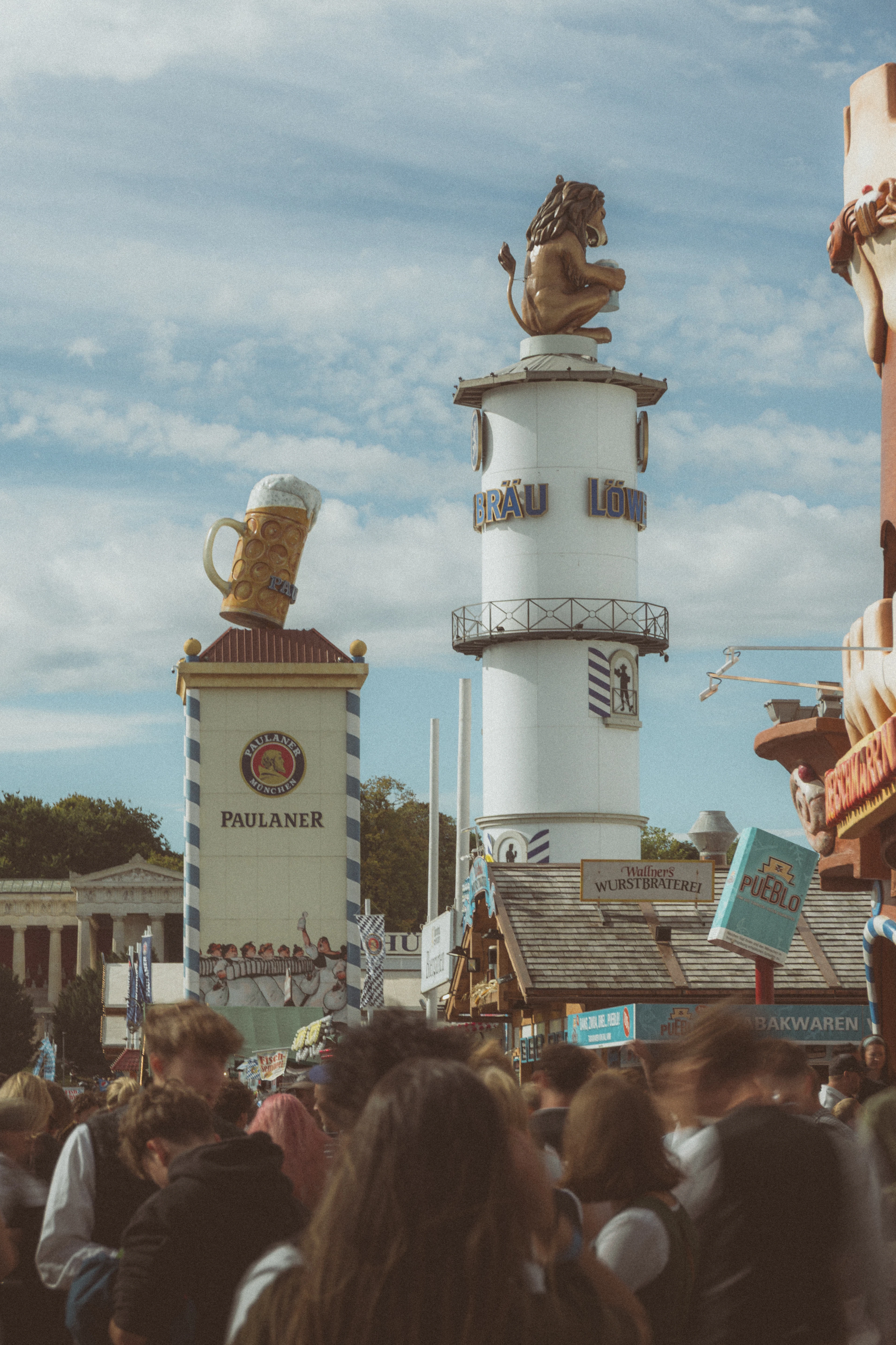 Crowds on the Oktoberfest grounds in Munich between the Paulaner tower topped by a giant beer stein and the Loewenbraeu tower with its lion.