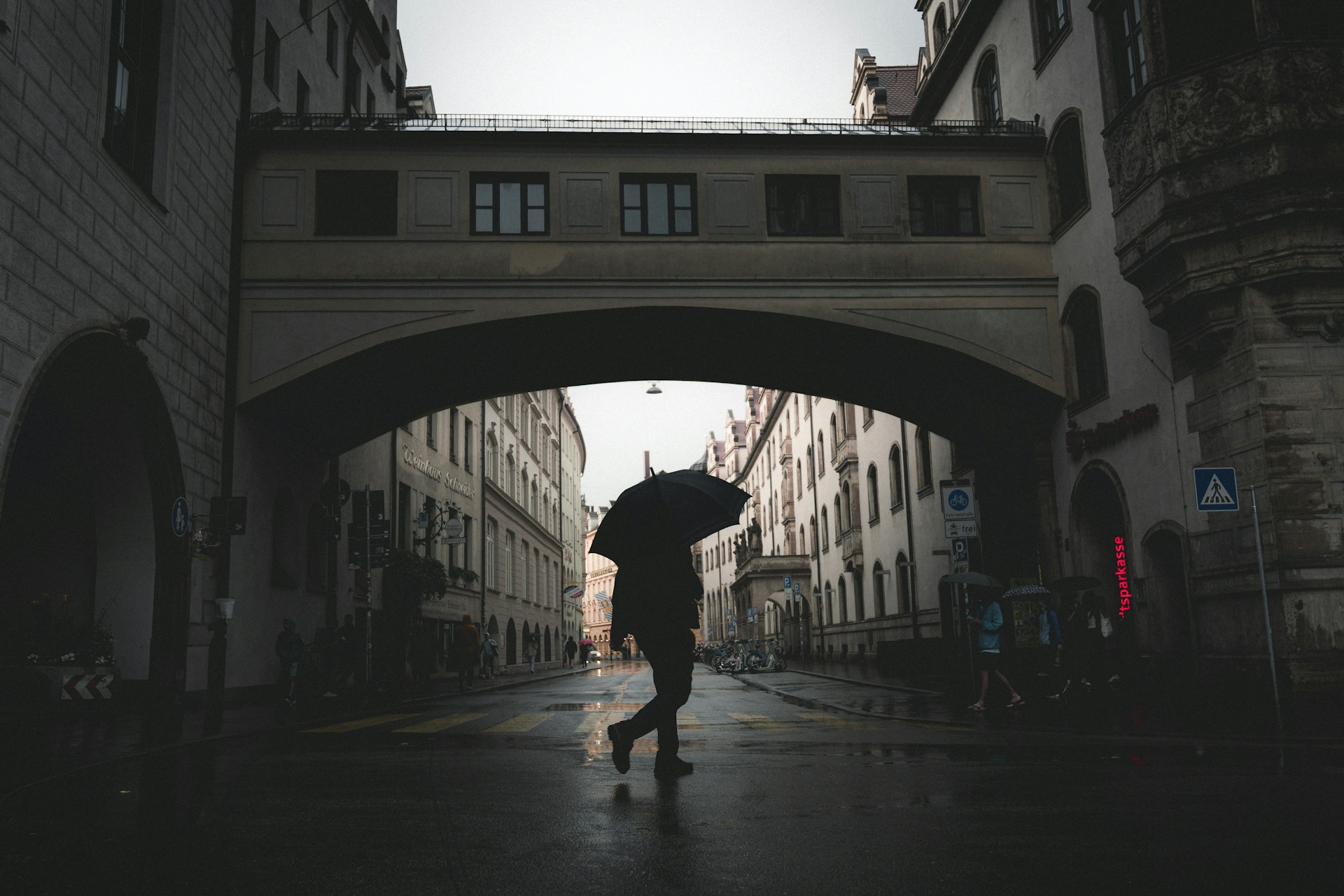 Person with umbrella walking under archway in rain.