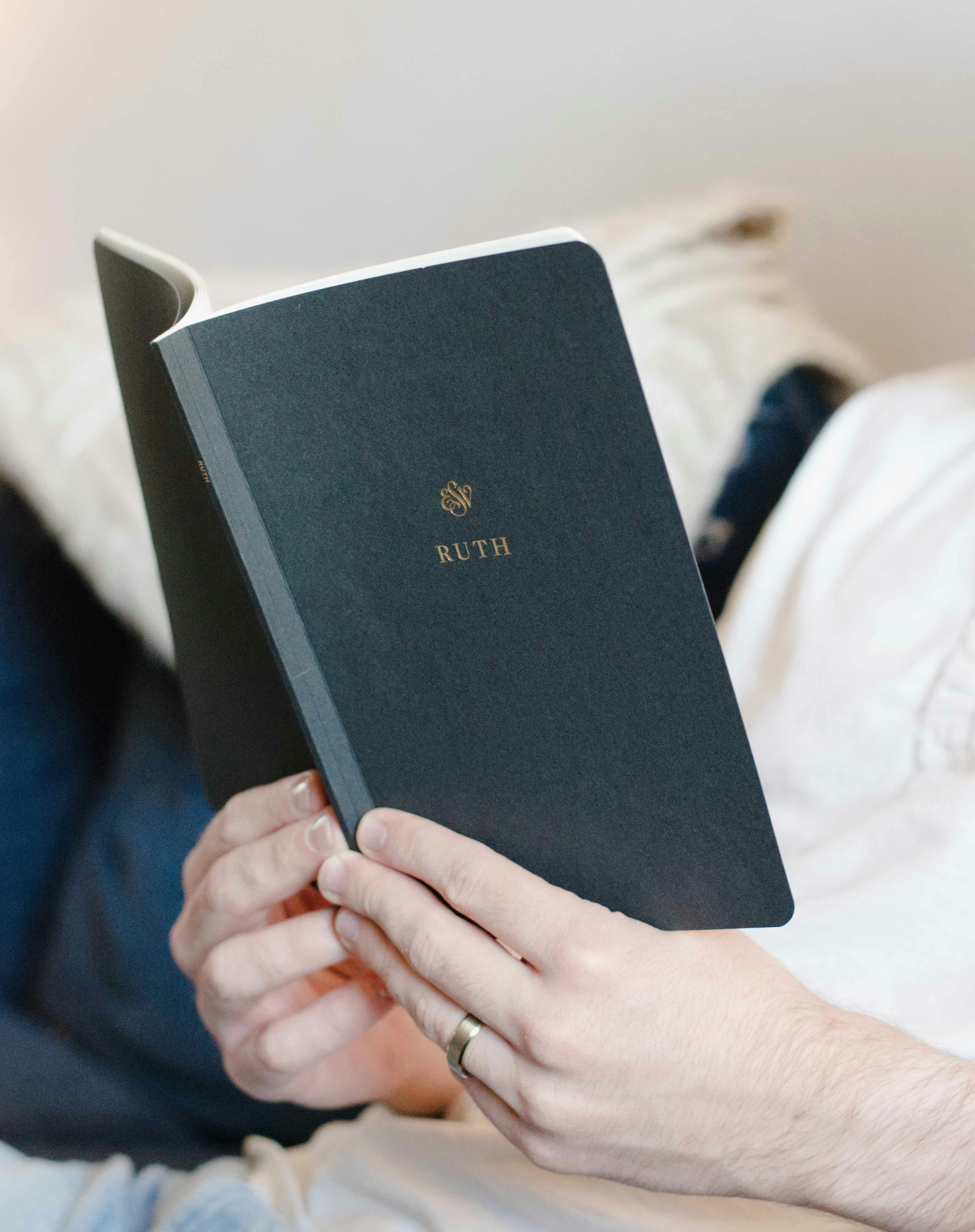 Person reading a dark green book with gold lettering.