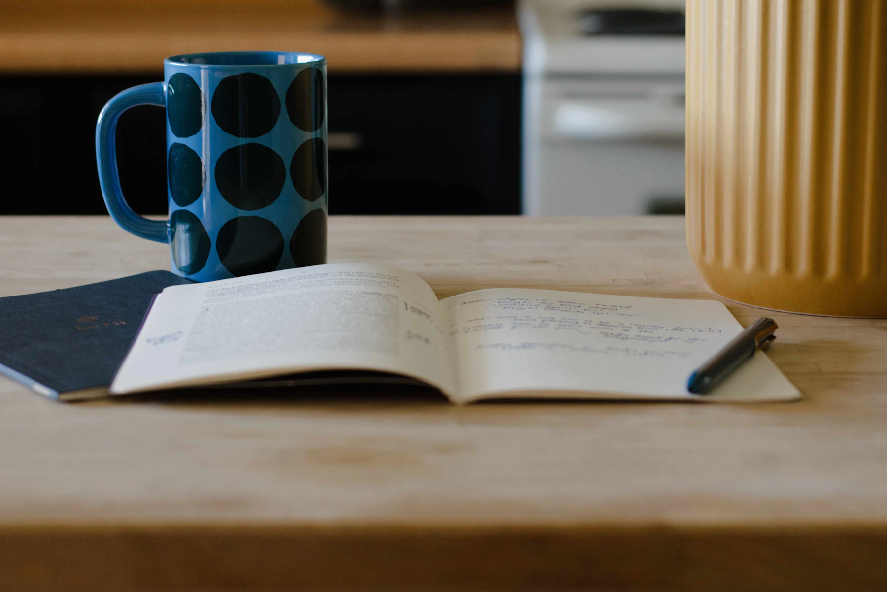 An open journal, pen, and mug on a wooden table in soft light