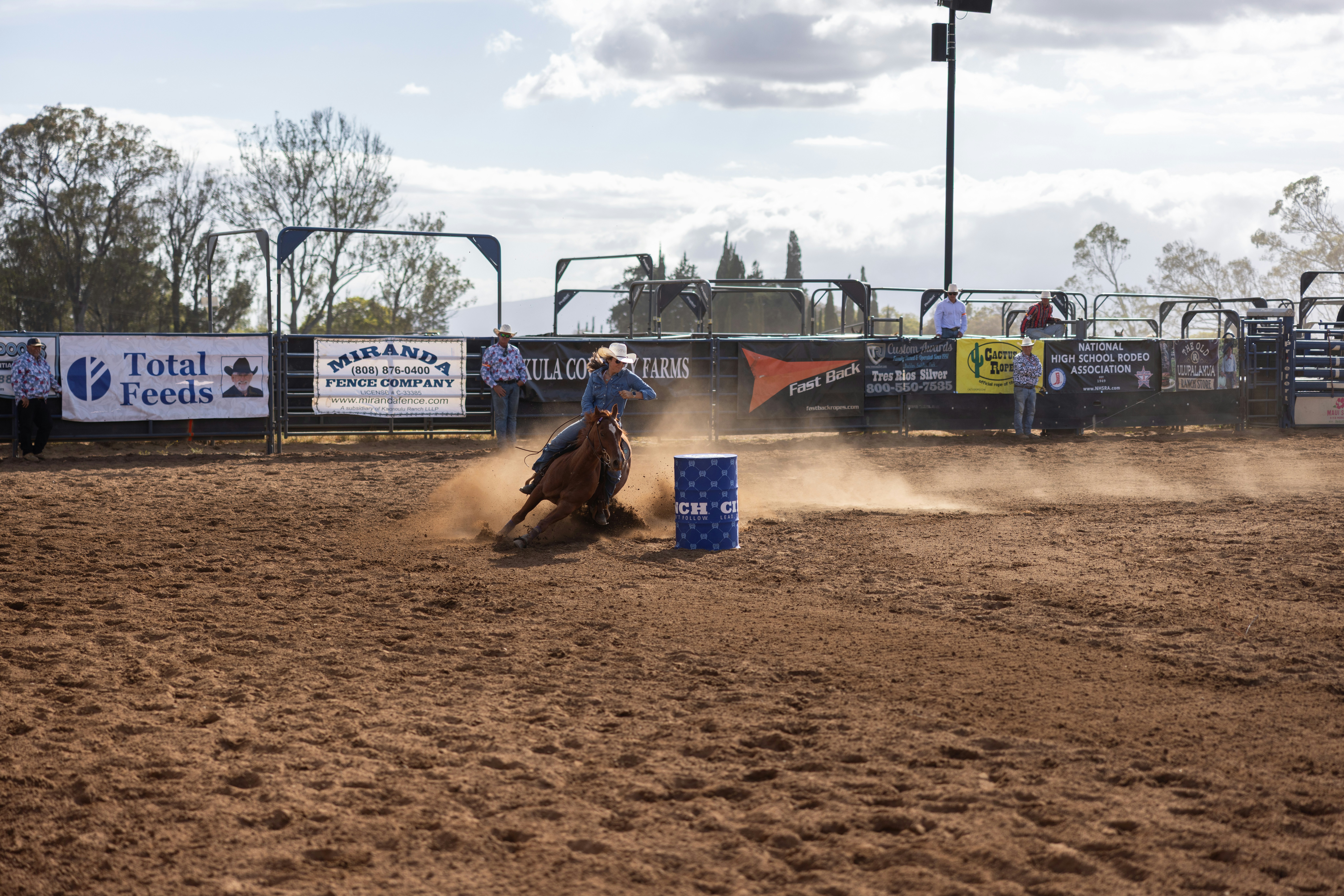 Cowgirl rounds barrel kicking up dust at rodeo.