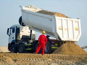 Worker in red supervises dump truck unloading sand