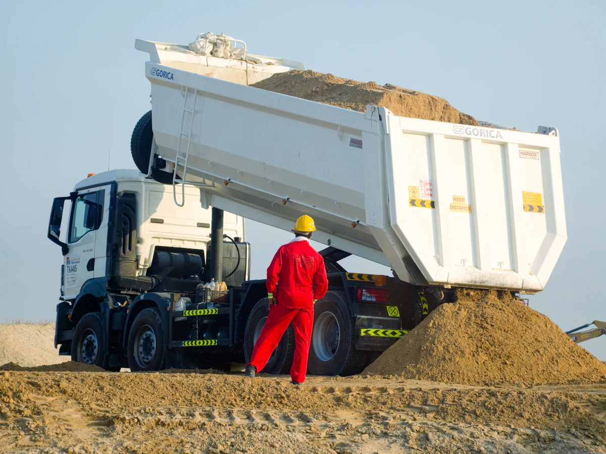 Medewerker in rode overall bij een witte kiepwagen onder een lichte lucht