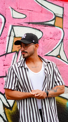 Man in striped shirt and baseball cap against graffiti wall.