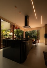 Modern kitchen island with pendant lights and greenery outside.