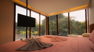 Bedroom with large windows overlooking lush green forest