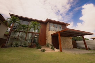 Modern wooden house with large windows and palm trees.