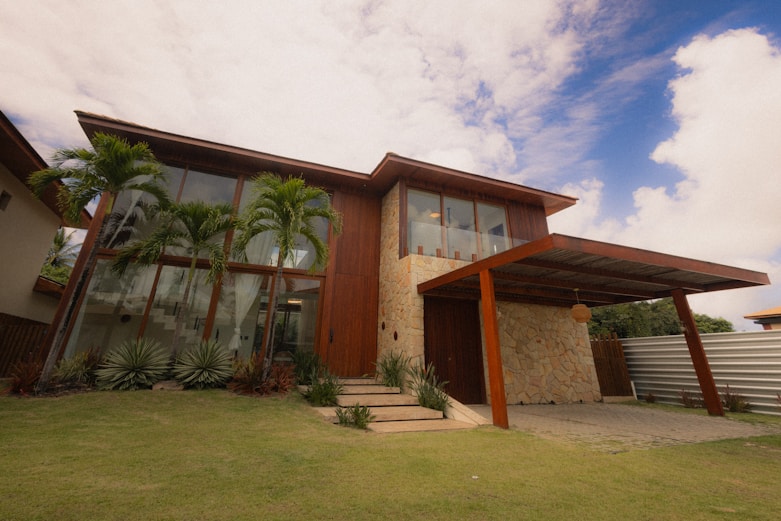 Modern wooden house with large windows and palm trees.