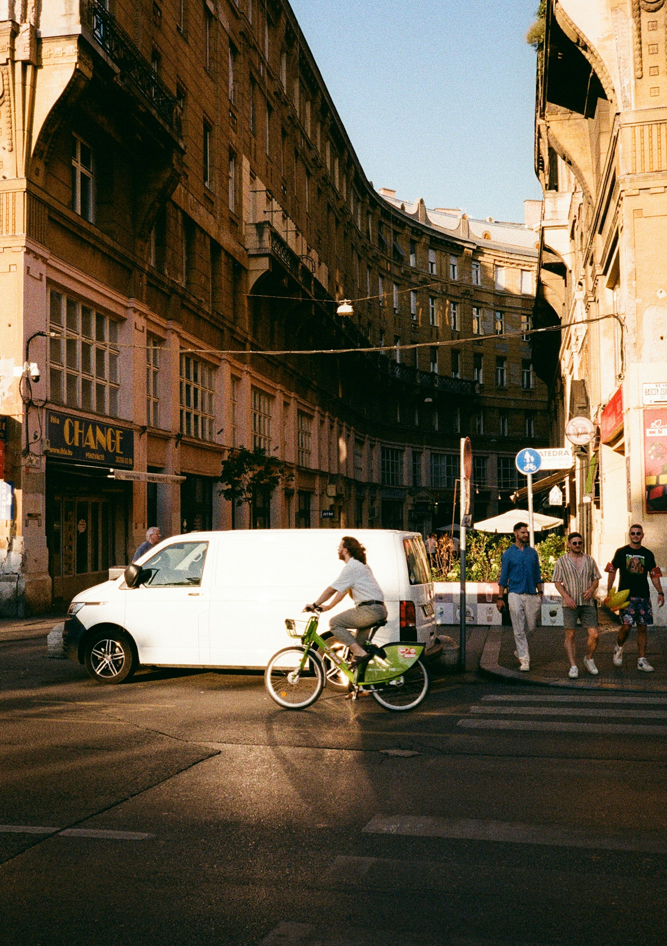 Cyclist crosses street in front of buildings and van