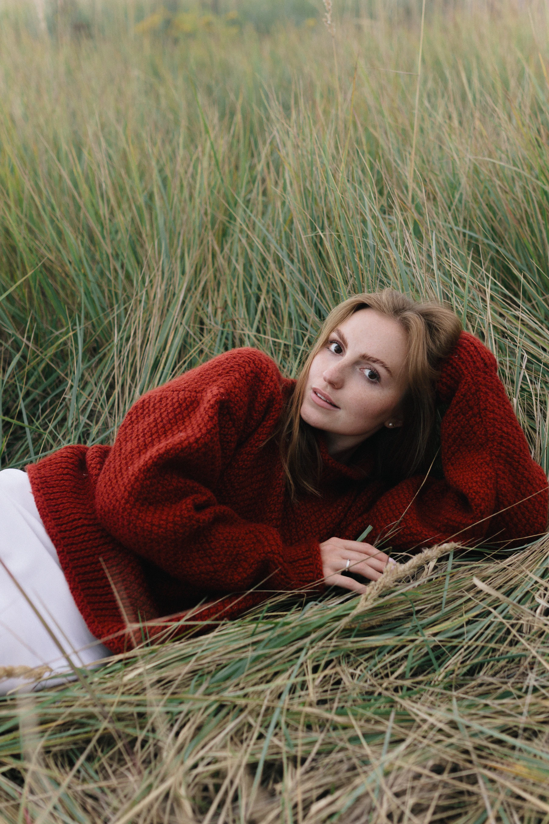 Woman in a chunky red knit sweater resting in tall dune grass