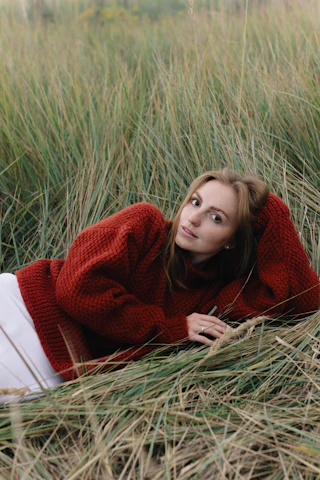 Woman in a chunky red knit sweater resting in tall dune grass