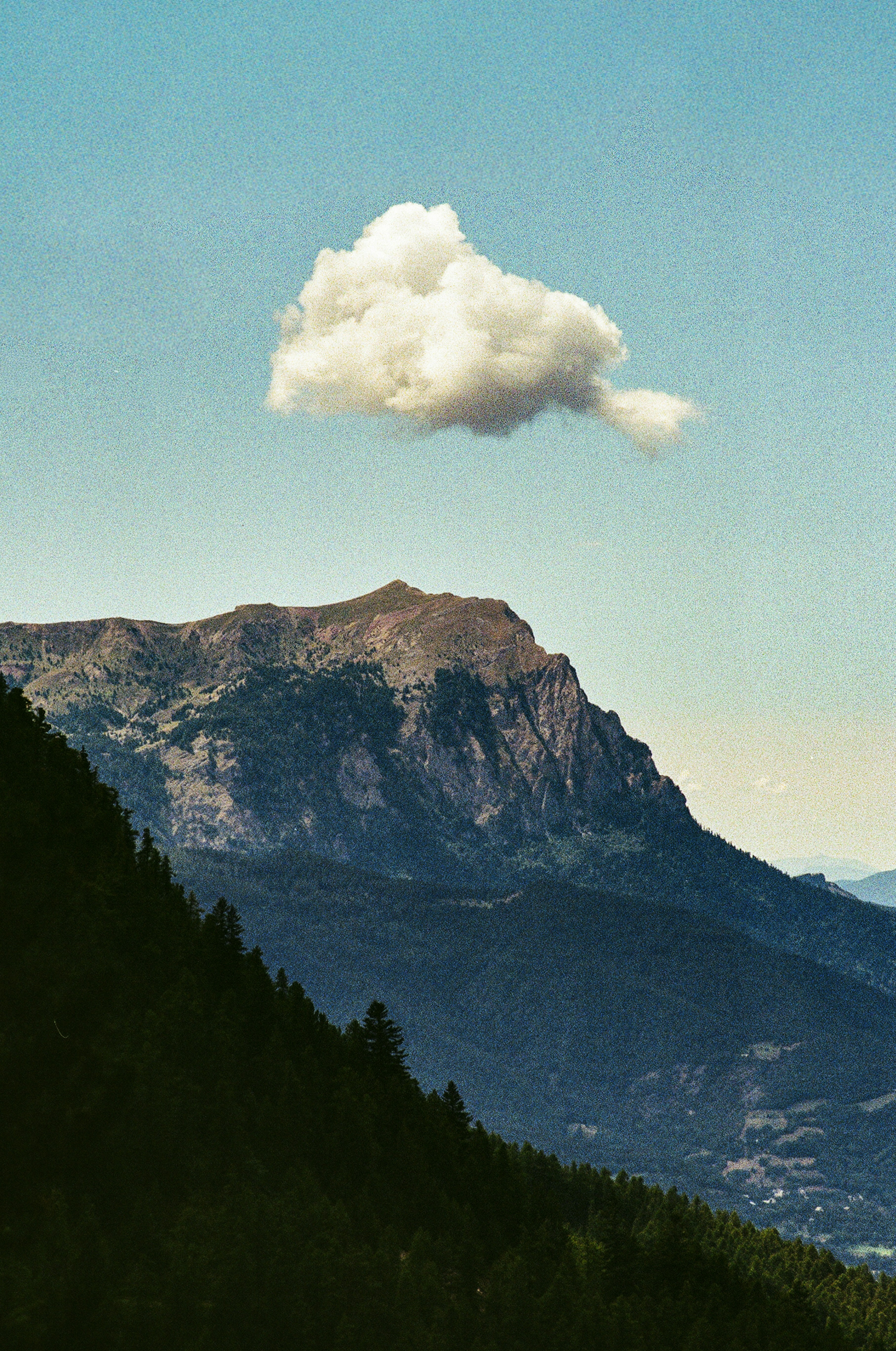 A single cloud floats above a rugged mountain peak.