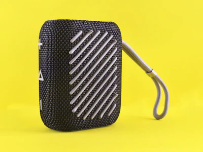 Black portable speaker with grey strap on yellow background