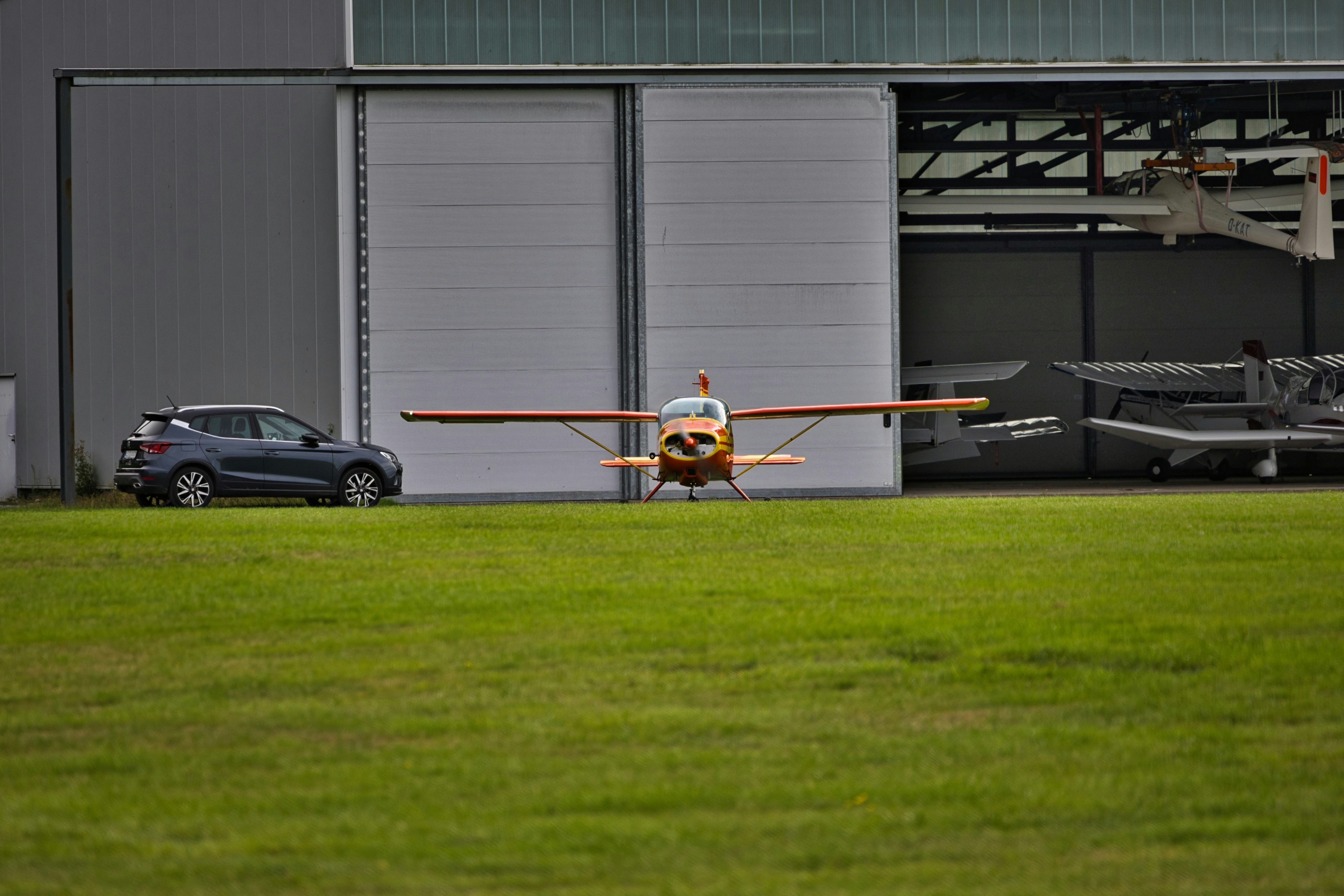 Small airplane parked outside hangar with car nearby