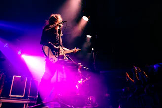 Musician playing guitar on a brightly lit stage.