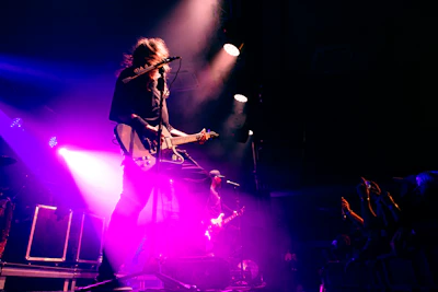 Musician playing guitar on a brightly lit stage.