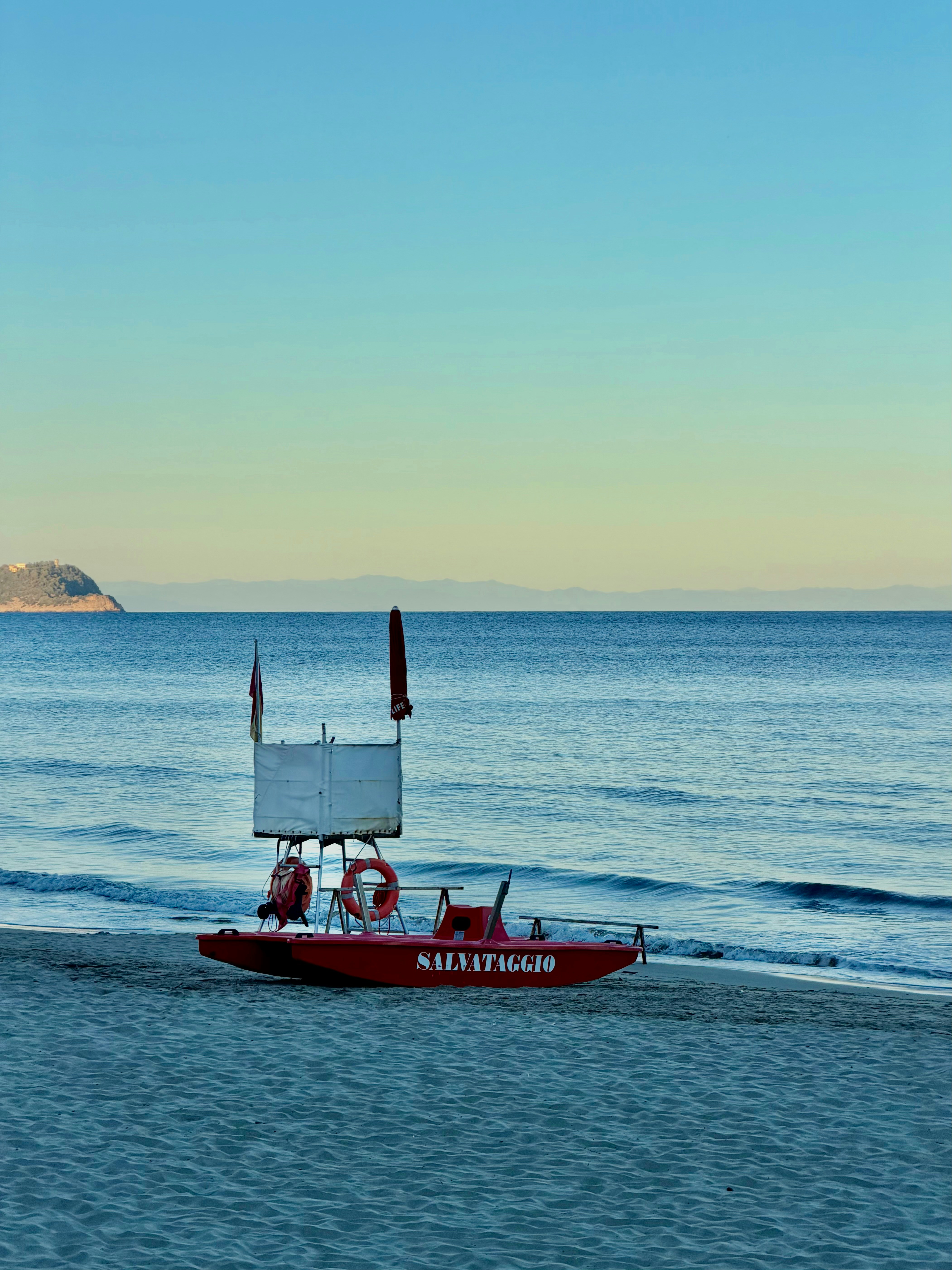 Red rescue boat on a sandy beach by the ocean.