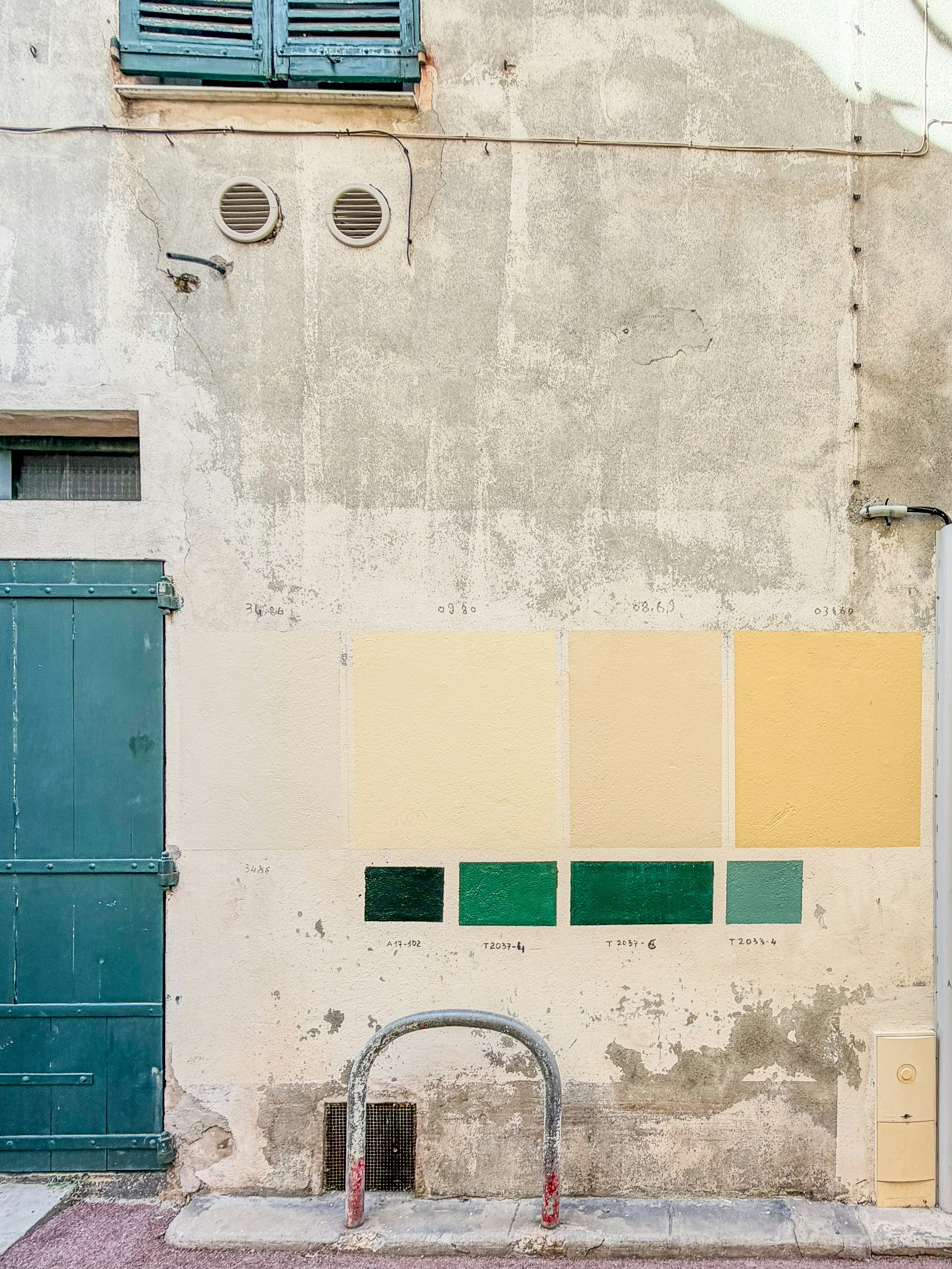 Paint swatches on a weathered wall with teal door.