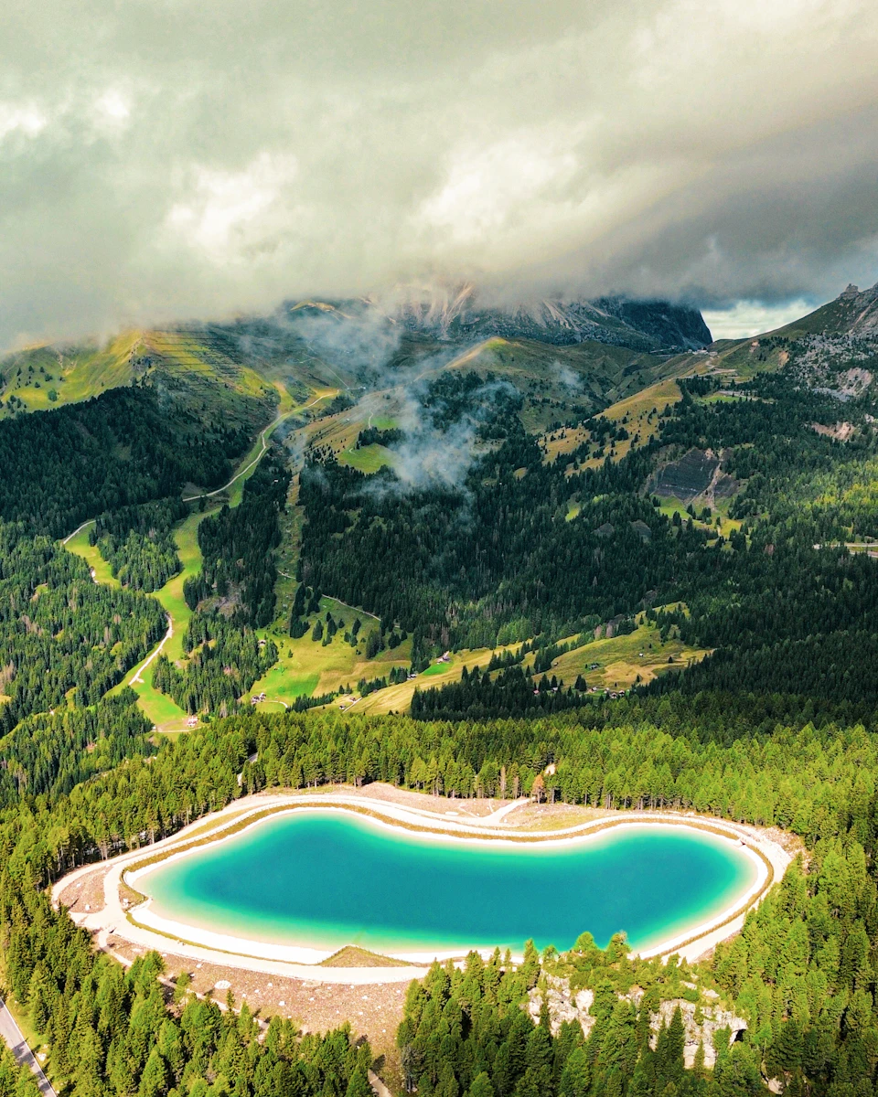 Aerial view of turquoise lake surrounded by lush greenery and towering mountainous landscape