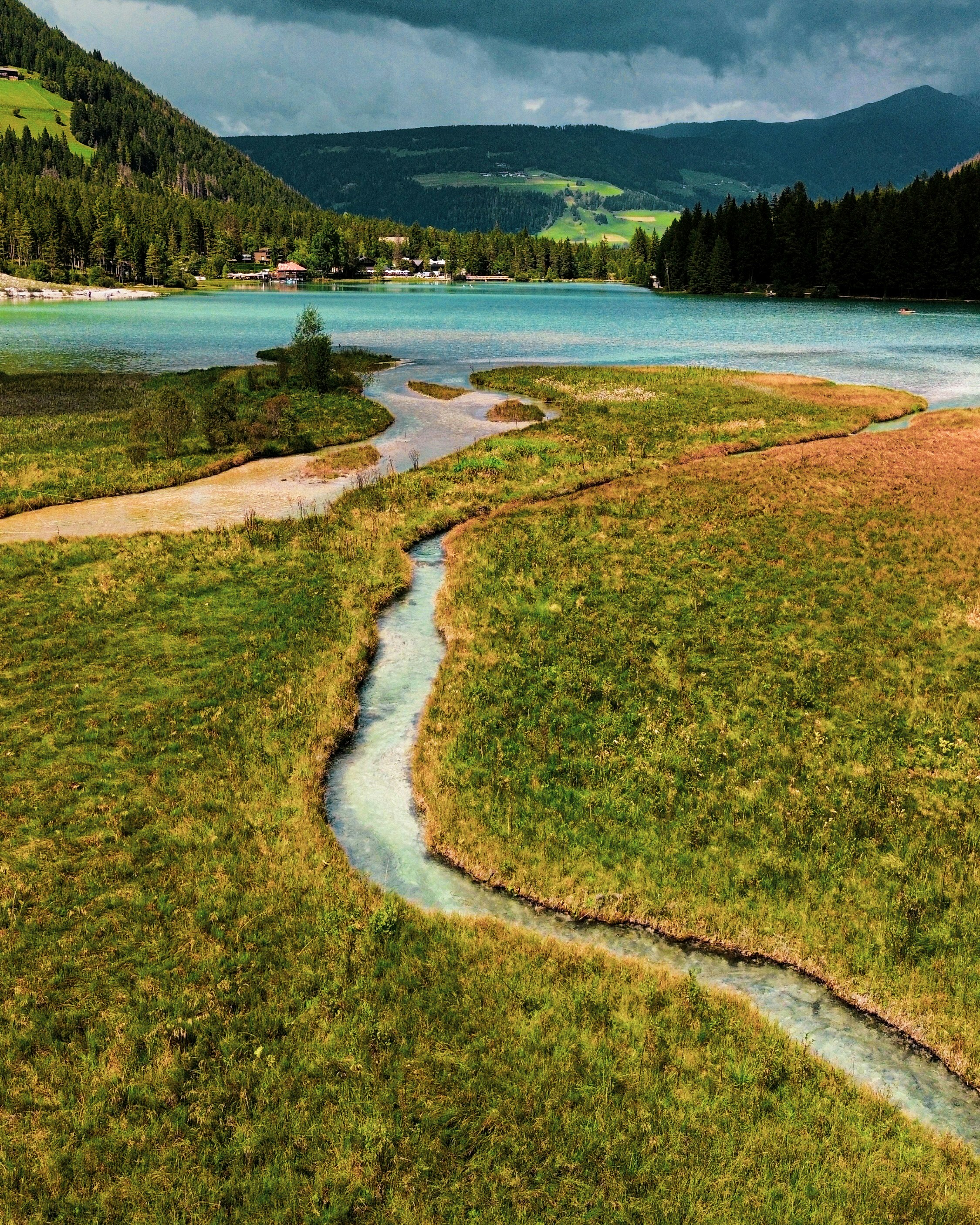 Pradera cubierta de hierba con un arroyo sinuoso que conduce a un lago.
