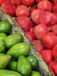 Green avocados and red pomegranates in crates