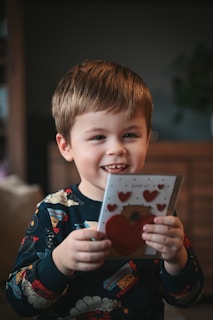 A smiling young boy holds a valentine's day card.