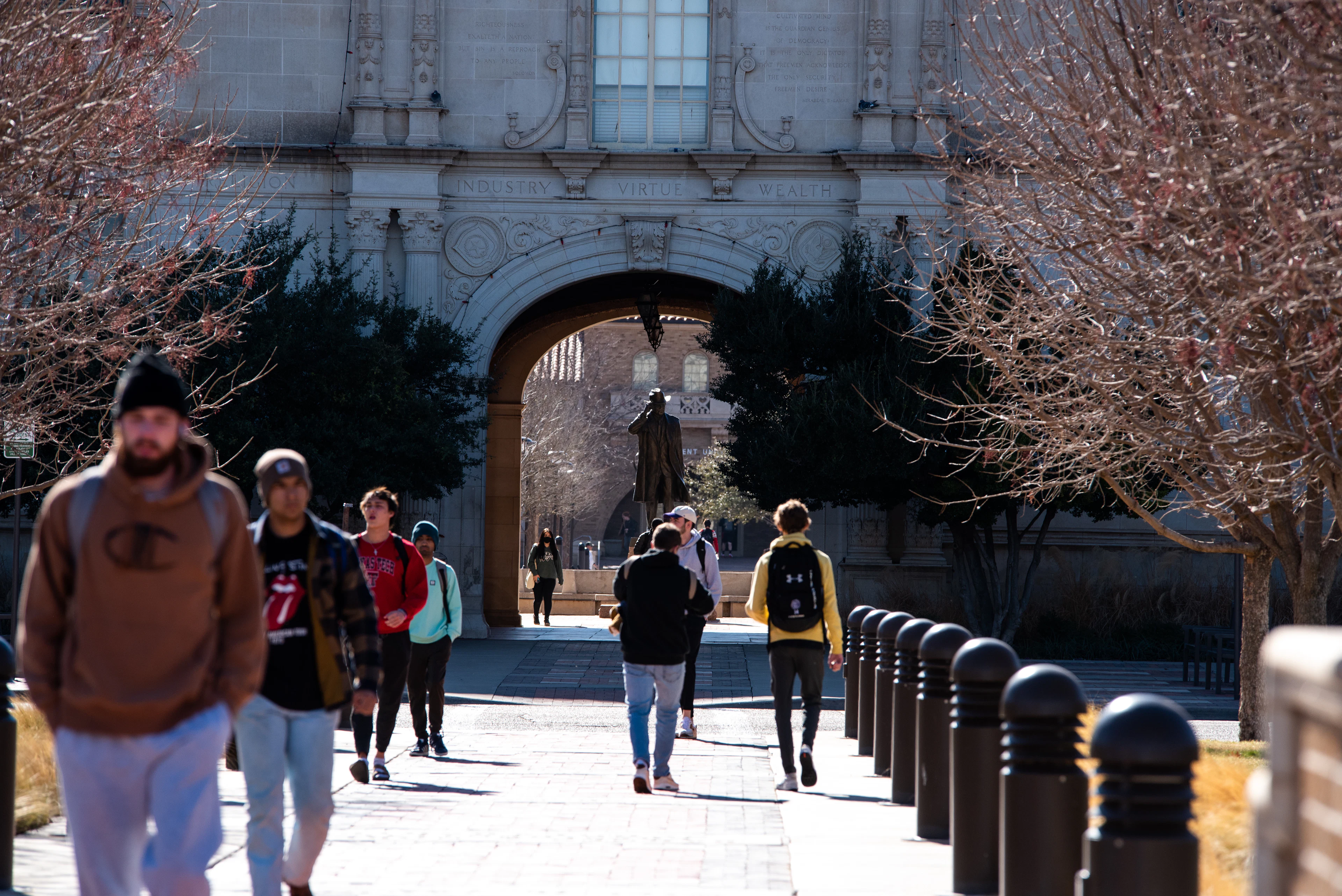 Students walking through a stone university archway on a bright winter day.
