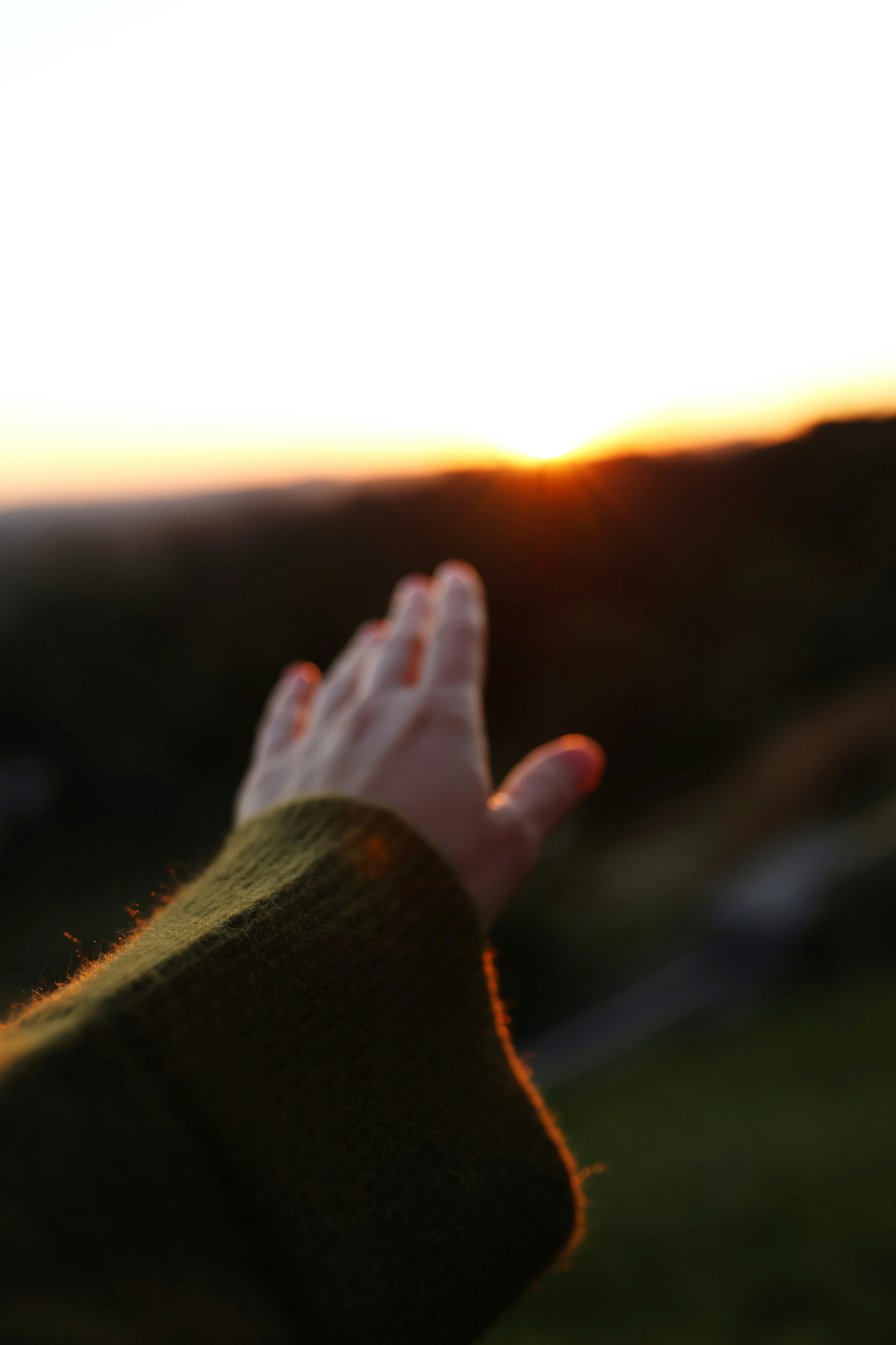Hand reaching towards the sunset over hills