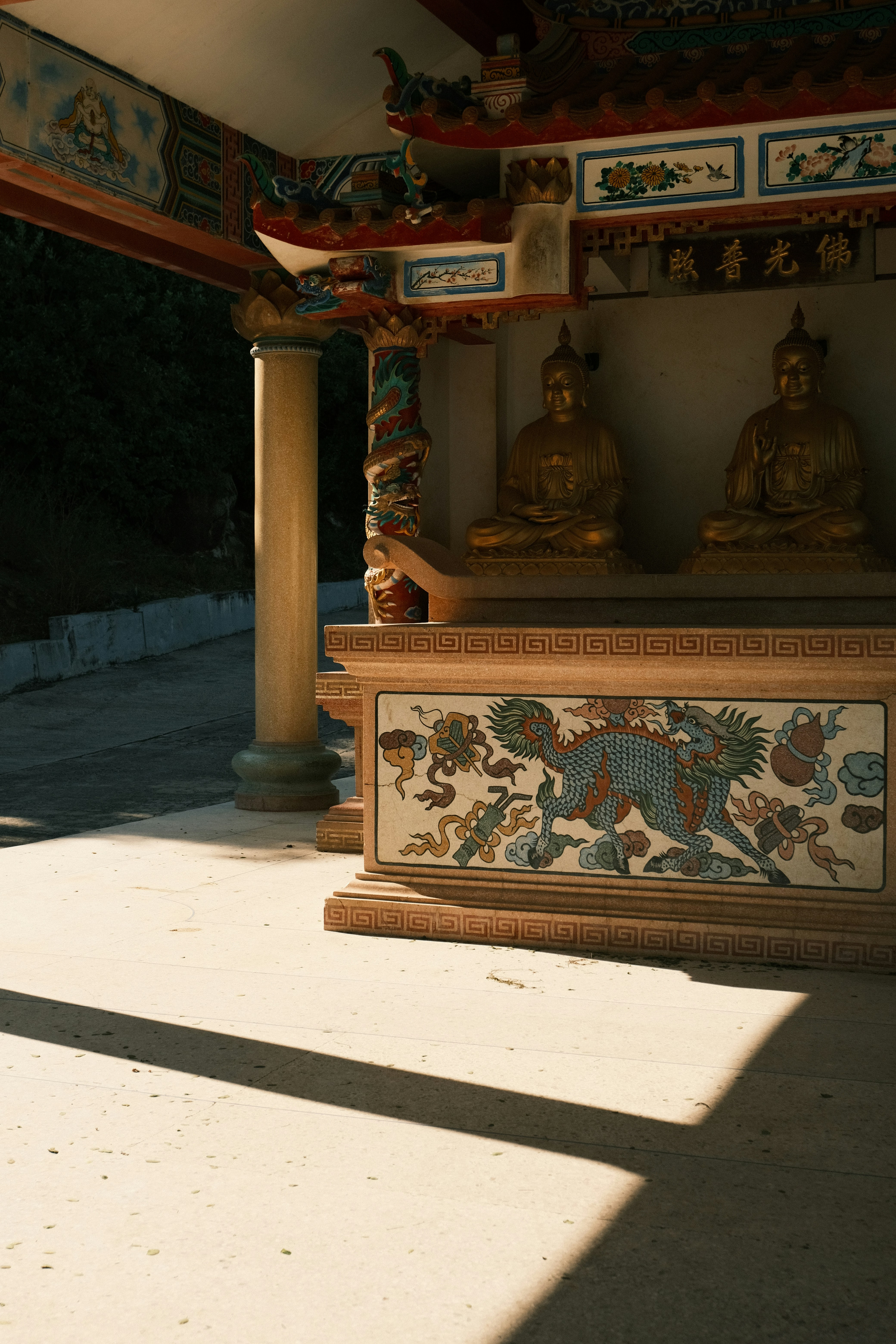 Two golden buddhas sit in ornate shrine with dragon mosaic.