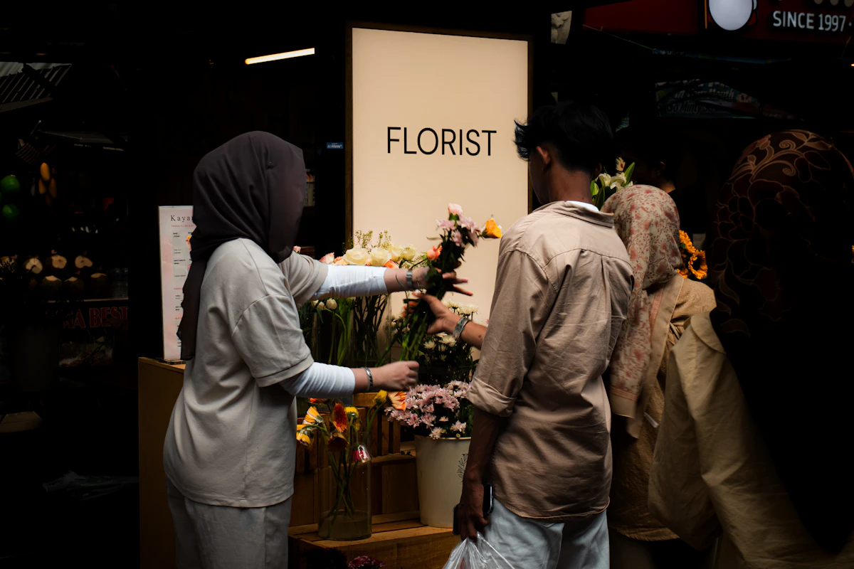 Une fleuriste remettant un bouquet de fleurs violettes et vertes à un client dans sa boutique