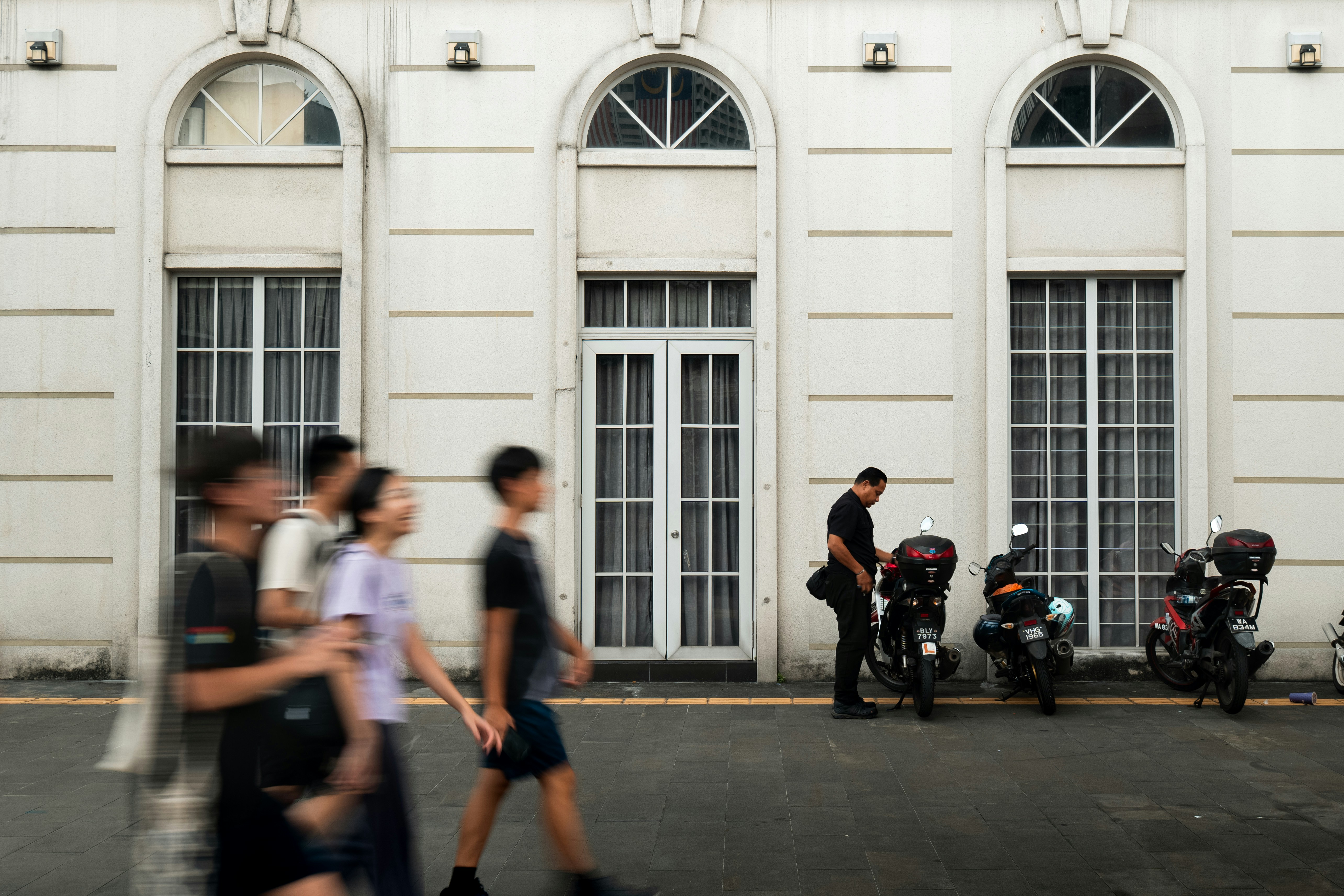 People walk past parked motorcycles outside building.